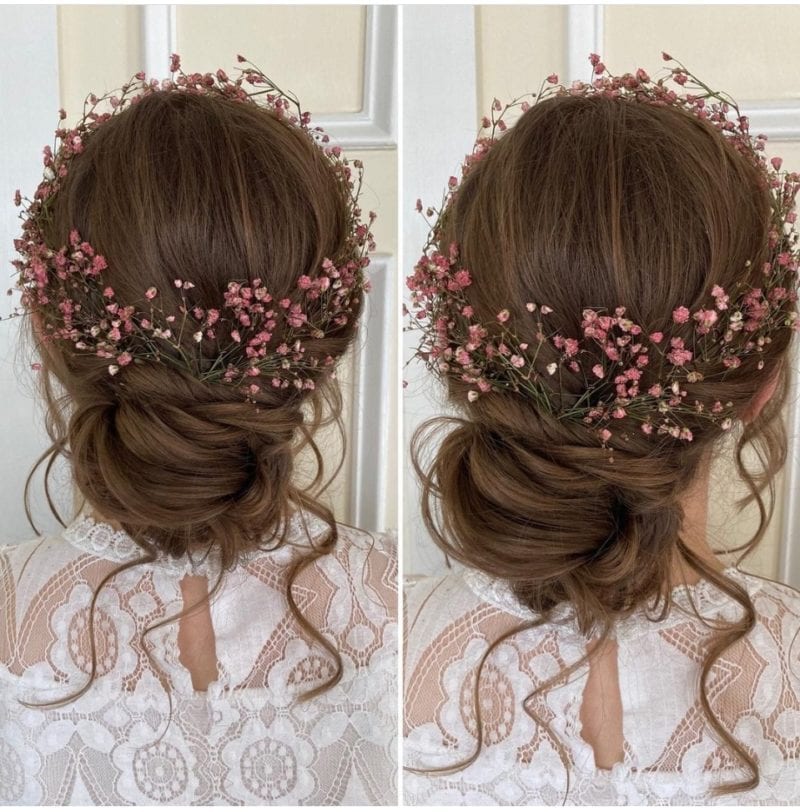 Elegant bridal hairstyle featuring soft curls and pink floral accessories.